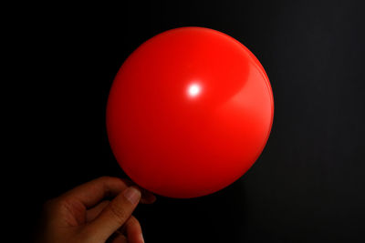 Close-up of hand holding red balloons against black background