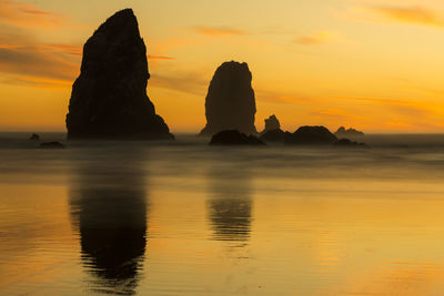 Silhouette rock formation in sea against sky during sunset