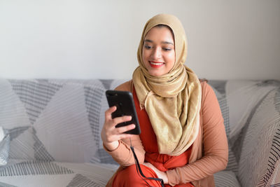 Smiling young woman using smart phone while sitting on laptop