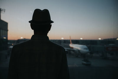 Rear view of silhouette man standing in city against sky during sunset