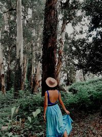 Full length of woman standing by tree trunk in forest