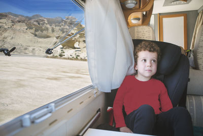  boy, sitting by the open window of his parked motorhome with a spectacular view.