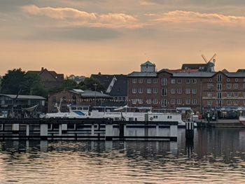 Buildings by river against sky during sunset