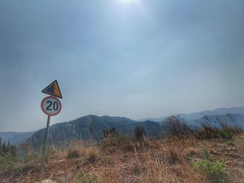 Road sign on field against sky