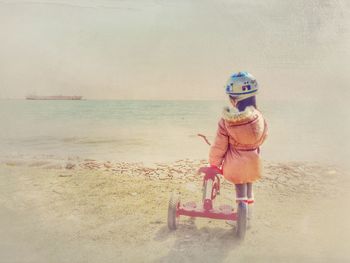 Rear view of girl standing by tricycle at seashore