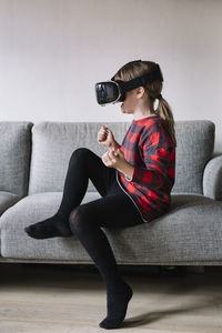 Girl sitting on the couch in the living room using virtual reality glasses