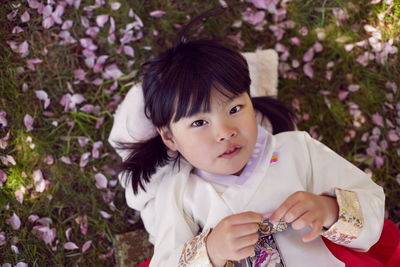 Korean girl child in a national costume lies on the back in a garden with cherry blossoms in spring