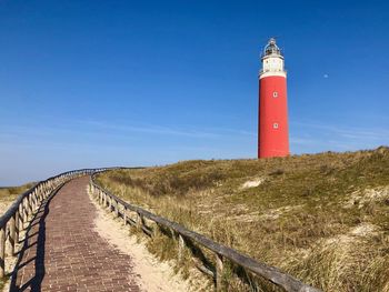 Lighthouse amidst buildings against clear blue sky