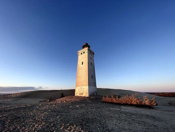 Lighthouse by sea against clear blue sky