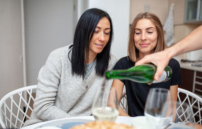 Cropped man pouring white wine in glass by friends sitting at table