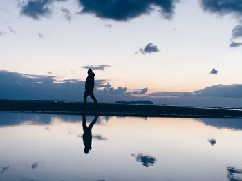 Silhouette person standing in lake against sky during sunset