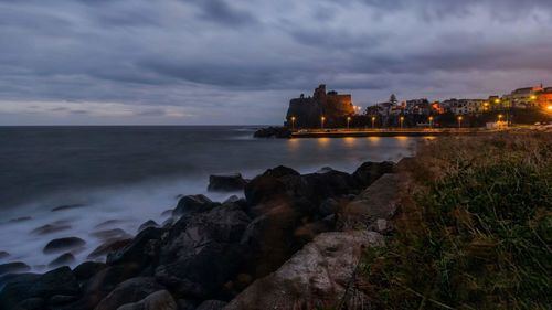 Sea by illuminated city against sky