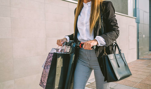 Midsection beautiful businesswoman holding push scooter on footpath