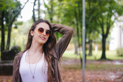 Portrait of smiling beautiful woman wearing sunglasses against trees