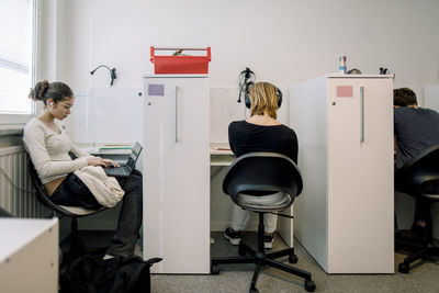 Male and female students using laptops sitting on chair in library at high school