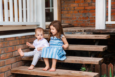 Girl sitting on bench against brick wall