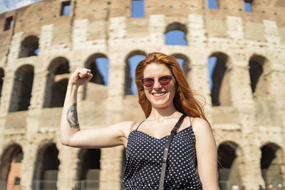 Cheerful young woman showing muscles near old attraction