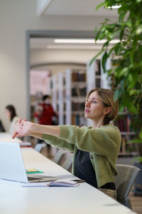 Woman getting second degree taking break from learning while studying online on laptop in library