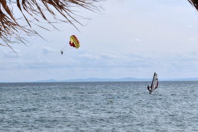 People enjoying water sports over sea against sky