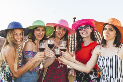 Portrait of smiling female friends toasting drinks while standing in balcony