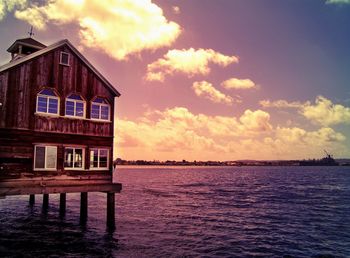 Scenic view of house by sea against cloudy sky at sunset