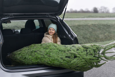 A girl sitting in the trunk with a christmas tree