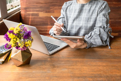 Midsection of woman using digital tablet while sitting by table in office