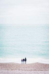 Rear view of people standing at beach against sky