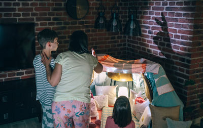 Mother and two children having fun playing with shadow puppets over brick wall at home pajama party