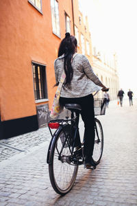 Rear view of woman standing with bicycle on cobbled street