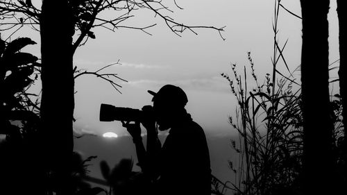 Silhouette man photographing against sky