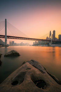 Bridge over river in city at sunset
