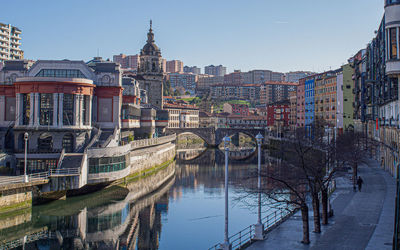 Bridge over river by buildings in city against sky