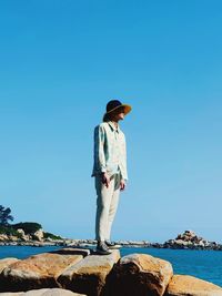 Side view of man standing on rock against clear sky