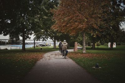 Rear view of people riding bicycle on footpath at park