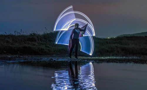 Woman standing by lighting paintings reflecting on lake