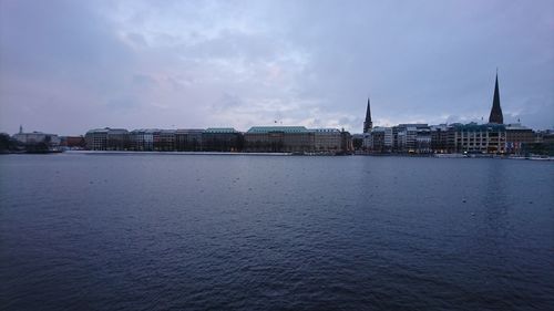 View of city at waterfront against cloudy sky