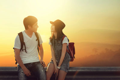 Couple sitting on railing by sunset