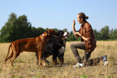 Man playing with dogs while standing on grassy land against sky