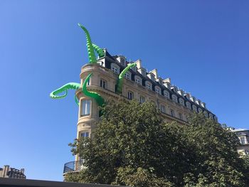 Low angle view of building with artificial octopus legs against blue sky