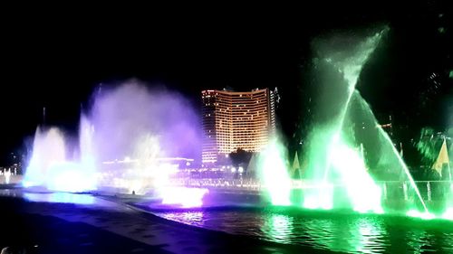 Illuminated fountain in city against sky at night