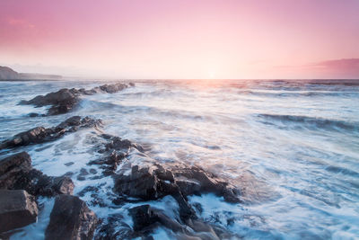 Scenic view of sea waves splashing on rocks during sunset