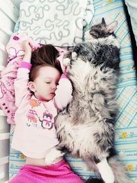 High angle view of cute girl lying with cat in crib at home