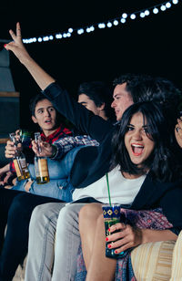 Portrait of cheerful woman lying on friends sitting at patio during night