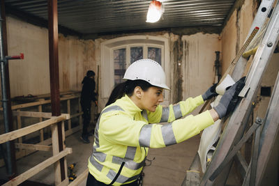 Female building contractor reading blueprint while working at site