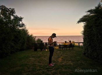 People standing by sea against sky during sunset