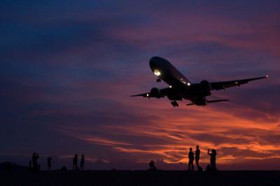 Silhouette of airplane flying against sky during sunset