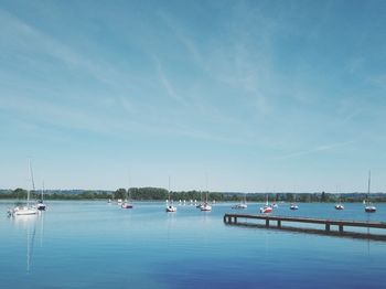 Sailboats moored in sea against blue sky