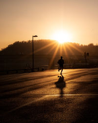 Rear view of silhouette person running on street against clear sky during sunset