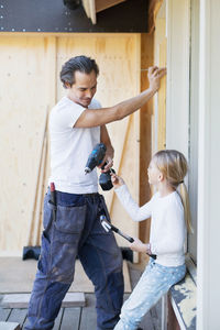 Daughter passing nail to father working on window frame of house being renovated